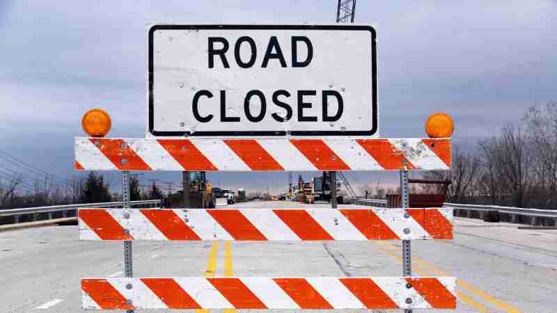A road closed sign with barricade highlights caution on a suburban highway., tags: closure - pexel